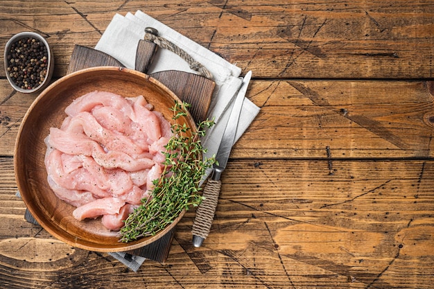 Tagliata di petto di tacchino di pollo crudo in un piatto di legno con timo Sfondo in legno Vista dall'alto Spazio di copia