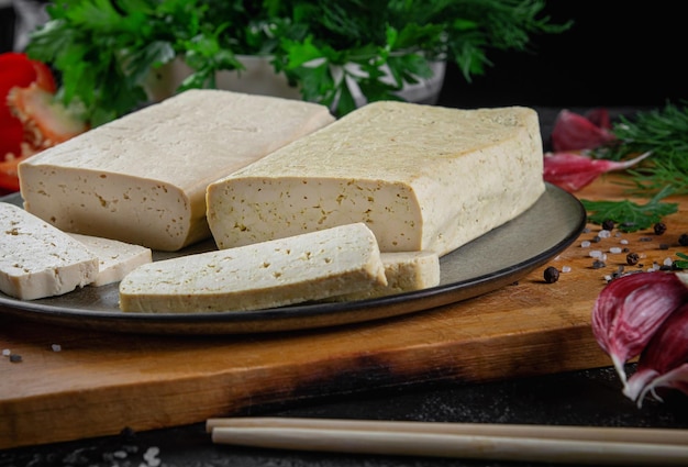 Tagliata di tofu al formaggio di soia su un tagliere con basilico, spezie e verdure