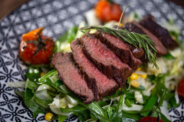 Tagliata succosa pezzo di manzo closeup su un piatto con erbe aromatiche e pomodori