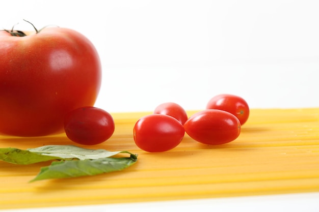 Tagliatella cruda degli spaghetti con i pomodori ed il basilico isolati nel fondo bianco