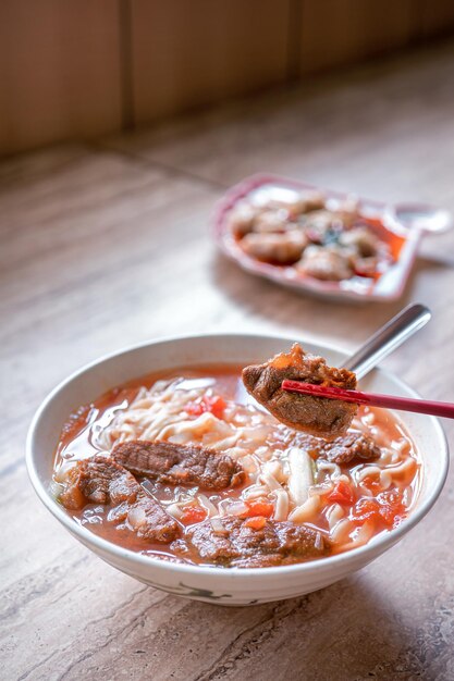 Tagliatella di manzo ramen di Taiwan pasto con salsa di pomodoro brodo in una ciotola su un tavolo di legno luminoso famoso cibo in stile cinese vista ravvicinata spazio copia