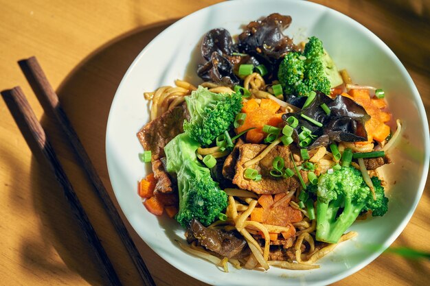 Tagliatelle al wok con manzo, verdure, salsa agrodolce e pepe di Sichuan. Fondo di legno. cucina cinese