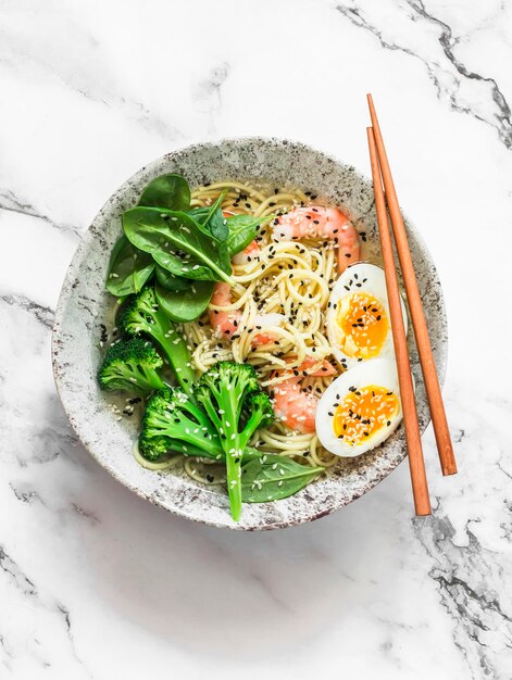 Tagliatelle all'uovo ramen per pranzo in stile asiatico con gamberetti, broccoli, spinaci e uovo sodo su uno sfondo chiaro vista dall'alto