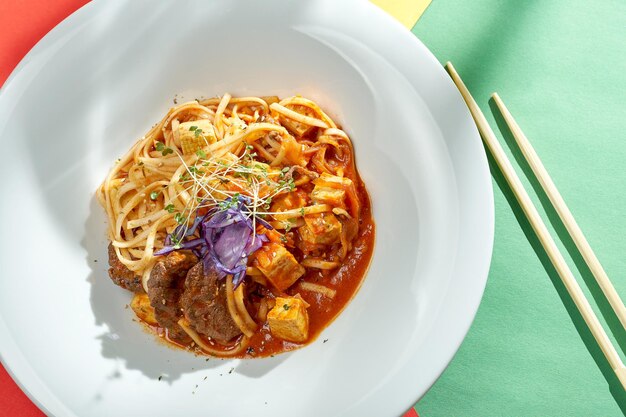 Tagliatelle asiatiche con salsa teriyaki, tofu e manzo in un piatto con sfondi luminosi. Messa a fuoco selettiva, luce dura