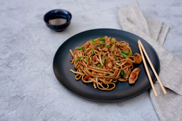 Tagliatelle asiatiche di udon con verdure di pollo e salsa teriyaki su un fondo di legno nero