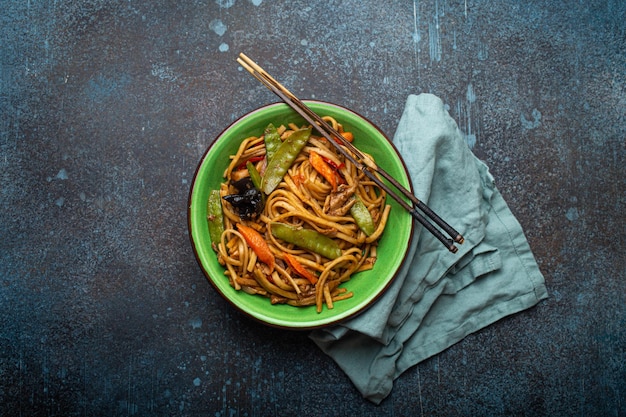 Tagliatelle asiatiche saltate in padella con pollo e verdure nella vista dall'alto della ciotola verde