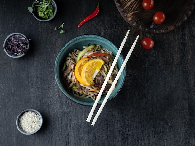 Tagliatelle asiatiche Yakisoba con carne di maiale in una ciotola su un ripiano in legno scuro