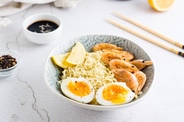 Tagliatelle cinesi con gamberetti fritti, uova sode e limone in una ciotola sul tavolo Cucina asiatica