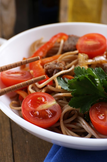 Tagliatelle cinesi con verdure e carne arrosto in una ciotola sul tovagliolo su fondo di legno