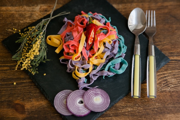 Tagliatelle colorate con spezie su tavola di legno, concetto di scena culinaria, primo piano vista dall'alto