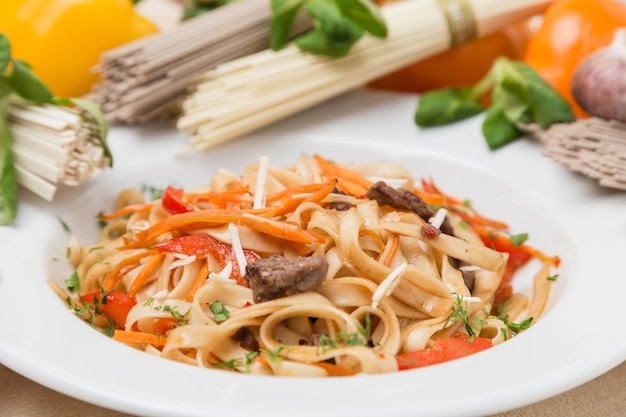 Tagliatelle con verdure e contorno sul piatto bianco