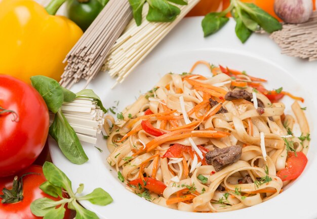 Tagliatelle con verdure e contorno sul piatto bianco