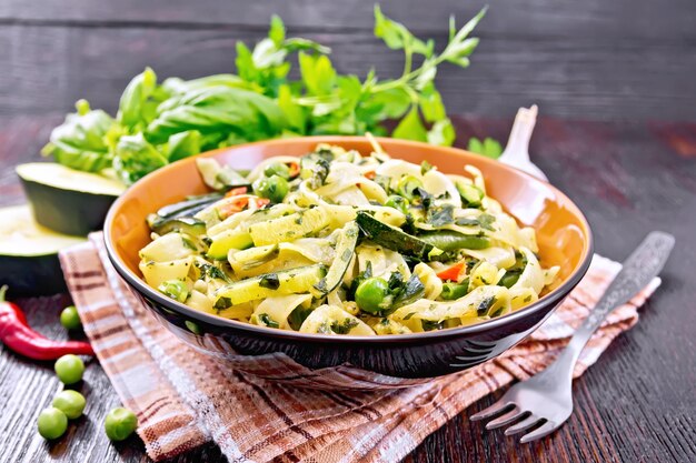 Tagliatelle con zucchine, piselli, fagioli di asparagi, peperoncino e spinaci in un canovaccio da cucina, aglio, forchetta e basilico su tavola di legno scuro