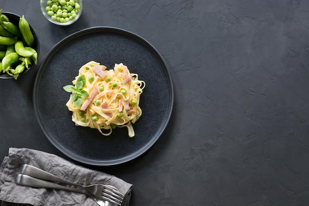 Tagliatelle di pasta con crema di piselli e pancetta su sfondo nero Delizioso pranzo mediterraneo Vista dall'alto Spazio per il testo