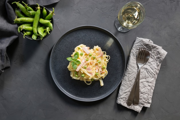 Tagliatelle di pasta con panna, piselli e pancetta sul nero. Delizioso pranzo mediterraneo.