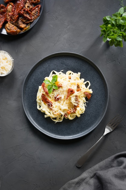 Tagliatelle di pasta con pomodori secchi e origano sul nero. Delizioso pranzo mediterraneo.