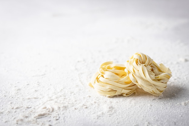 Tagliatelle di pasta italiana fatta in casa cruda cruda su un tavolo luminoso