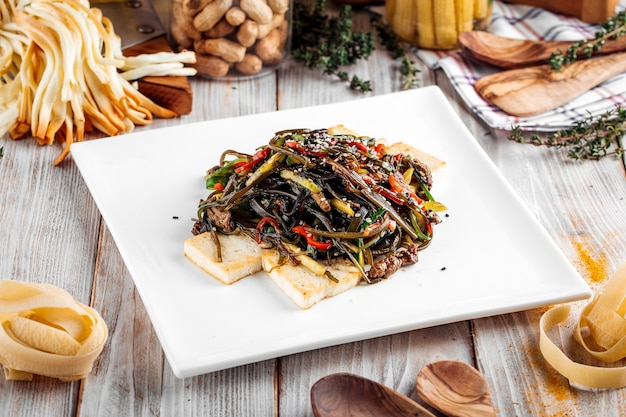 Tagliatelle di stile asiatico con carne di manzo e formaggio tofu in piatto quadrato