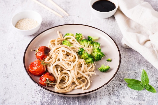 Tagliatelle di udon fritte in salsa di soia con pomodori broccoli e semi di sesamo su un piatto sul tavolo