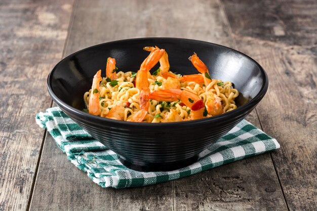 Tagliatelle e gamberetti con le verdure in ciotola nera sulla tavola di legno