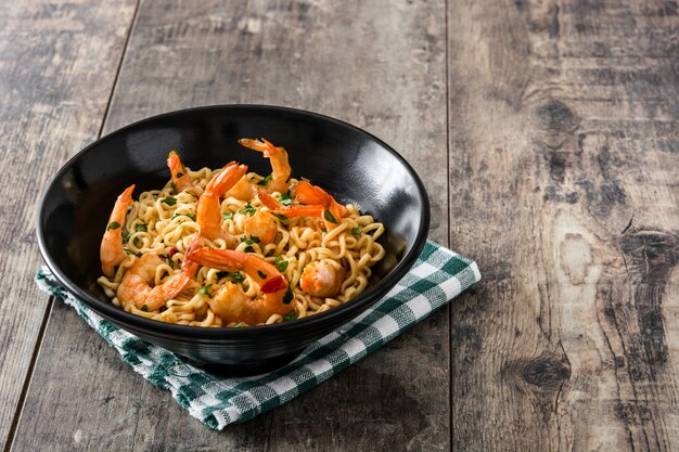 Tagliatelle e gamberetti con le verdure in ciotola nera sulla tavola di legno