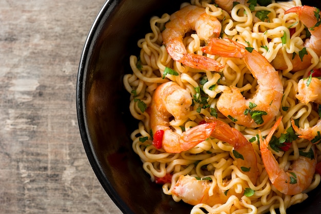 Tagliatelle e gamberetti con le verdure in ciotola nera sulla tavola di legno