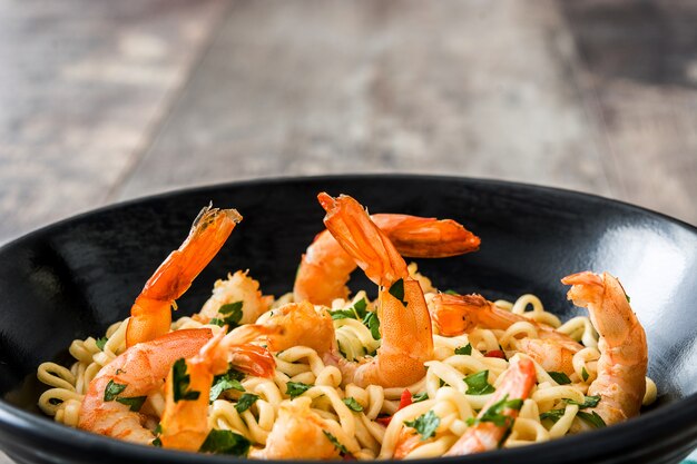 Tagliatelle e gamberi con le verdure in ciotola nera sulla fine di legno della tabella in su