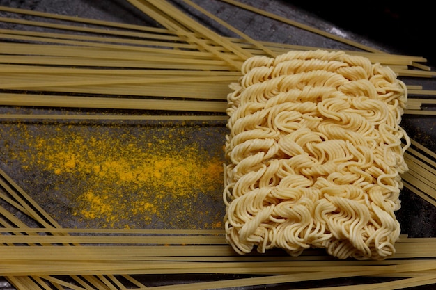 Tagliatelle e spaghetti istantanei crudi con spezie gialle su sfondo scuro Vista del primo piano dall'alto