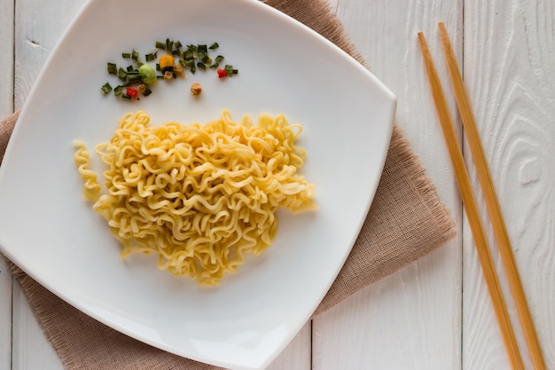 Tagliatelle e spezie istantanee sulla zolla e bacchette su un bianco