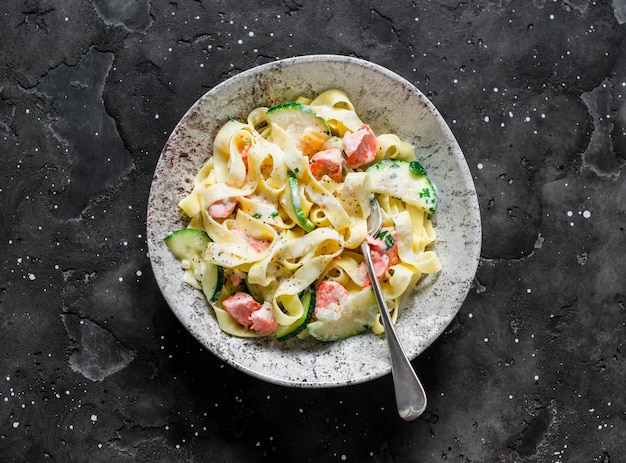 Tagliatelle fresche con salmone e zucchine in salsa di panna su sfondo scuro vista dall'alto