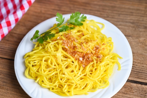 Tagliatelle gialle sulla piastra bianca e sullo sfondo di legno tagliatelle istantanee tagliatelle gialle vermicelli di riso cibo con aglio fritto e coriandolo