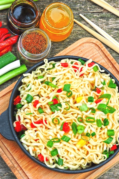 Tagliatelle in stile cinese in una padella di ghisa su un supporto di legno. Tagliatelle cinesi con verdure e peperoncini. Spaghetti vegetariani piccanti con verdure.