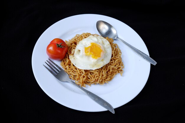 Tagliatelle istantanee fritte con uovo e pomodoro su un piatto, su sfondo nero