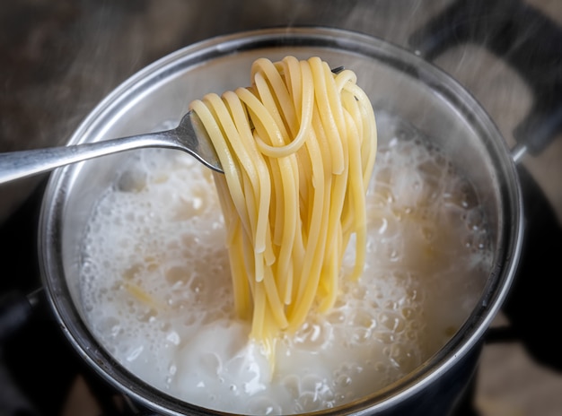 Tagliatelle o spaghetti gialli che cucinano in pentola di acqua bollente.