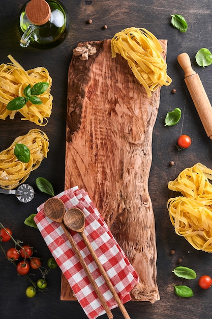 Tagliatelle. Pasta fatta in casa, foglie di basilico, farina, pepe, olio d'oliva, pomodorini e mattarello e coltello da pasta su fondo di legno vecchio scuro. Concetto di cibo. Modello. Orizzontale con copia spazio.