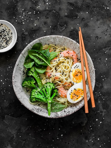 Tagliatelle ramen con gamberetti, broccoli, spinaci e uova sode su sfondo scuro vista dall'alto Delizioso pranzo in stile asiatico