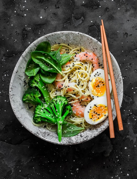 Tagliatelle ramen con gamberetti, broccoli, spinaci e uova sode su sfondo scuro vista dall'alto Delizioso pranzo in stile asiatico