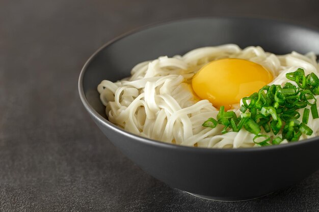 tagliatelle udon calde con uova e cipolla verde tritata ingredienti giapponesi su sfondo scuro vista laterale messa a fuoco selettiva