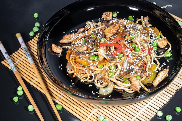 Tagliatelle Udon con carne, funghi e verdure Cosparse di semi di sesamo Arrosto di cibo asiatico su sfondo nero