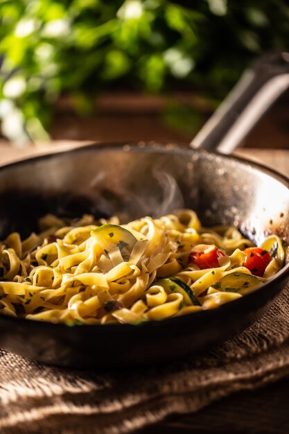 Tagliatelle vegetariane con zucchine e pomodori servite in una padella bollente.