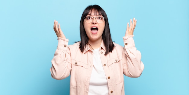 Taglie forti donna graziosa che si sente felice, stupita, fortunata e sorpresa, celebrando la vittoria con entrambe le mani in aria