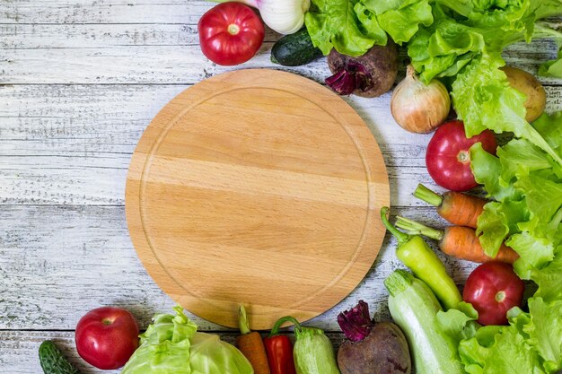 Tagliere circolare e verdure su fondo di legno bianco Mangiare sano