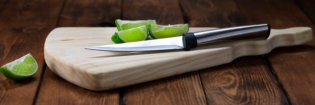 Tagliere in legno chiaro con un coltello e pezzi di lime su un tavolo di legno