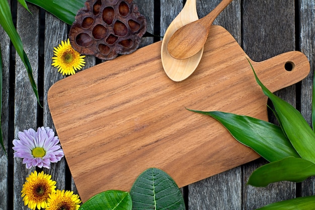 Tagliere in legno con foglie verdi tropicali, fiori rosa e gialli e cucchiaio