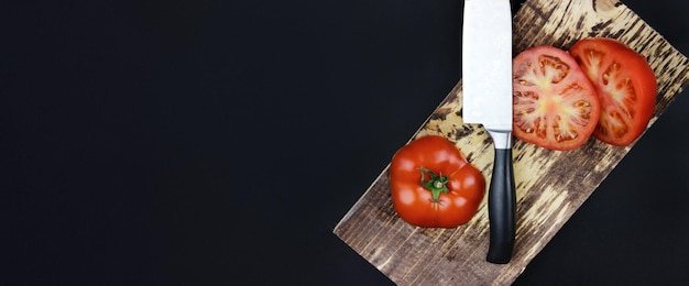 Tagliere in legno con pomodori a pezzetti Il coltello taglia a metà un pomodoro Pomodoro Fresco Tagliato