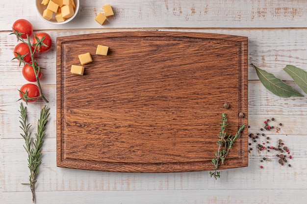 Tagliere quadrato in legno con bordo pomodorini fette di formaggio e spezie su sfondo bianco mockup con spazio per la copia per la vista dall'alto del testo