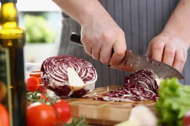 Taglio del cavolo rosso con il coltello sul tagliere in cucina