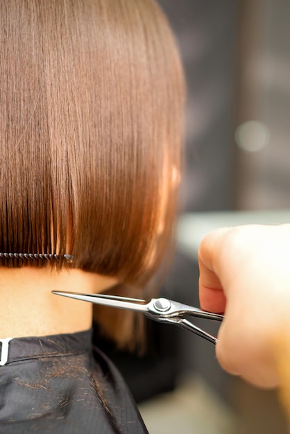 Taglio di capelli di capelli corti di giovane donna bianca per mano di un parrucchiere in un parrucchiere vista posteriore da vicino