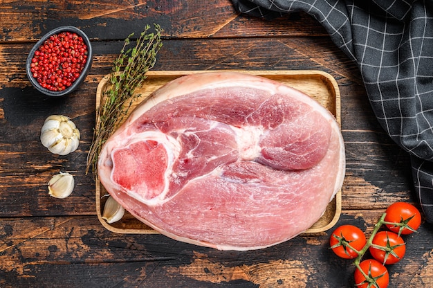 Taglio di stinco di maiale crudo, gamba su un tagliere. Carne fresca di fattoria. Superficie scura in legno. Vista dall'alto.