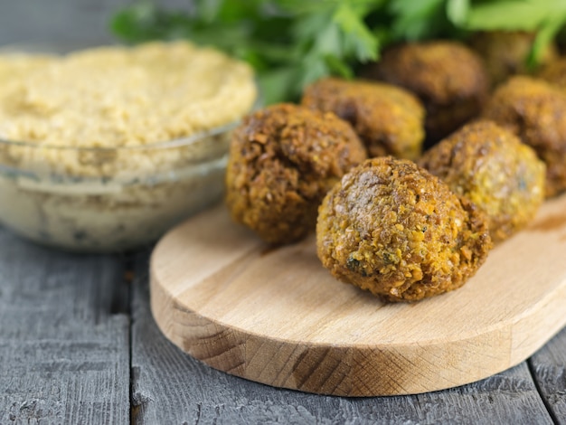 Tahina della pasta in una ciotola di vetro e falafel su un tagliere su una tavola di legno